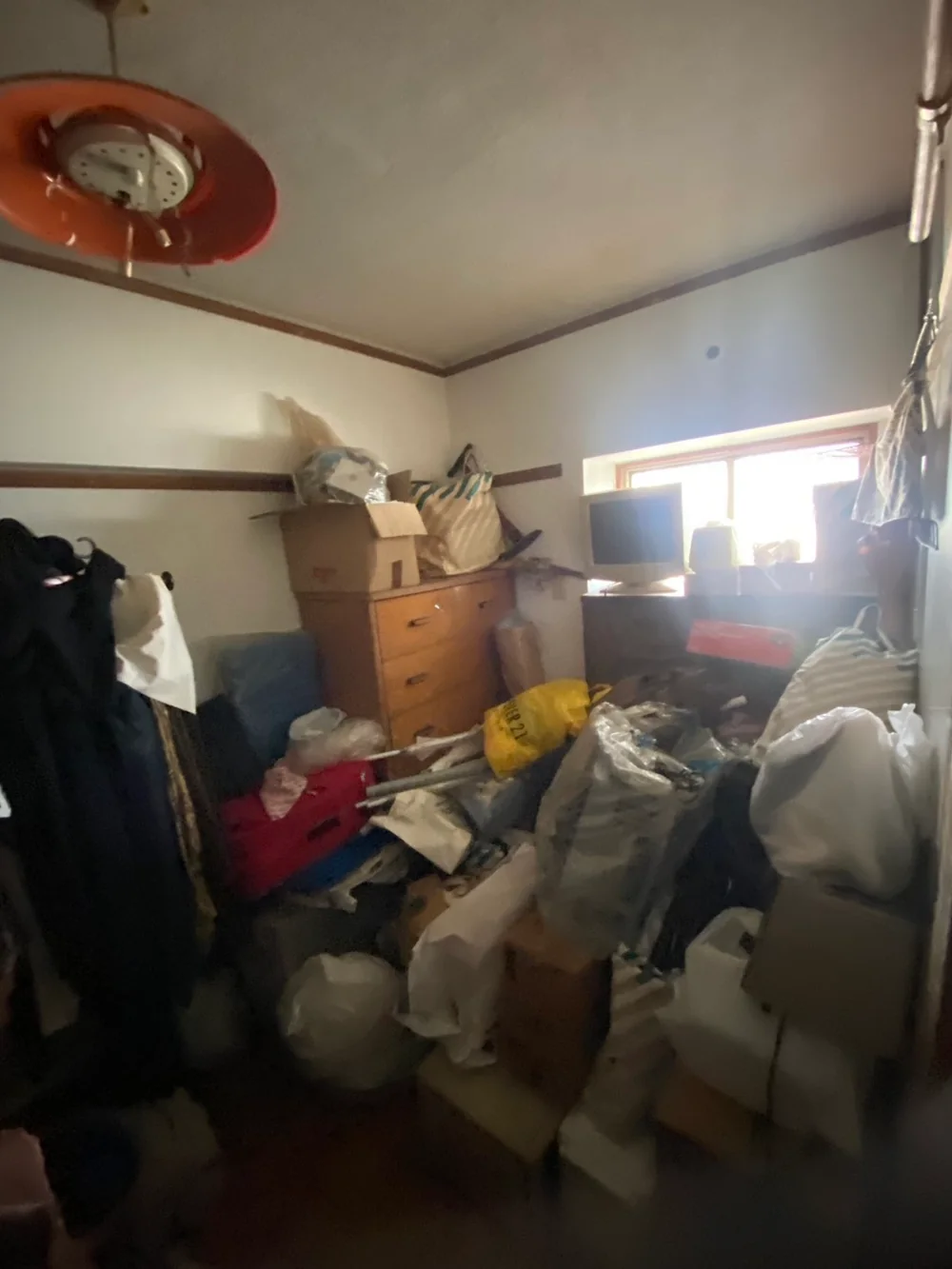 福岡県のゴミ屋敷片付け・汚部屋片付け | 九州片付け隊 福岡市の3LDKの一室で、タンスやモニター、段ボール、袋入りの家財が重なった作業前の室内