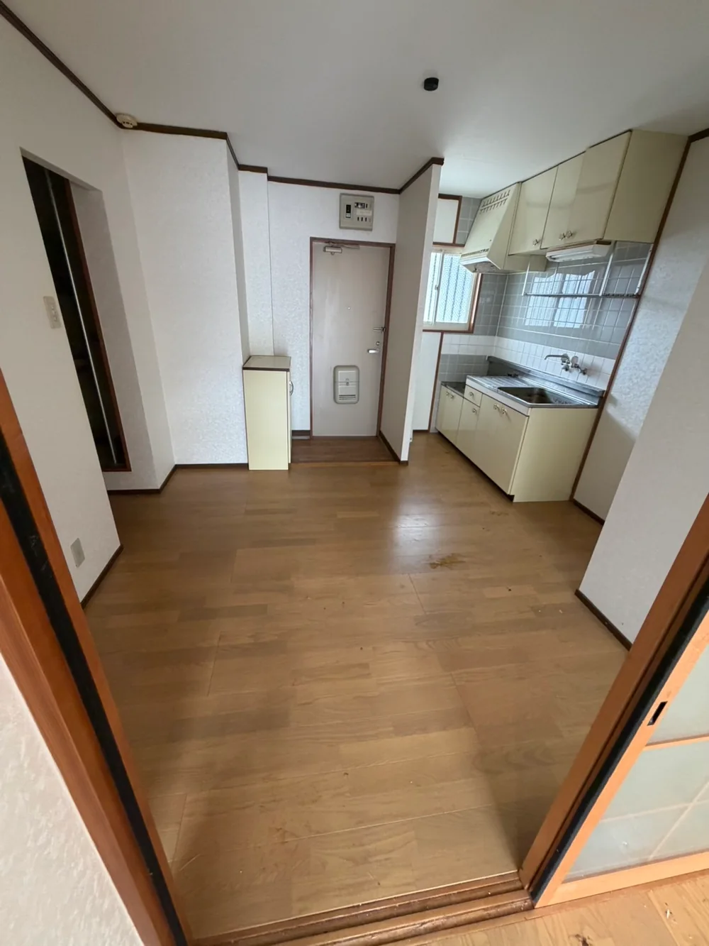 福岡県のゴミ屋敷片付け・汚部屋片付け | 九州片付け隊 福岡市南区の同じアパートで、生活ごみと大型冷蔵庫を搬出し、玄関からキッチンの床と通路が見える状態になった室内